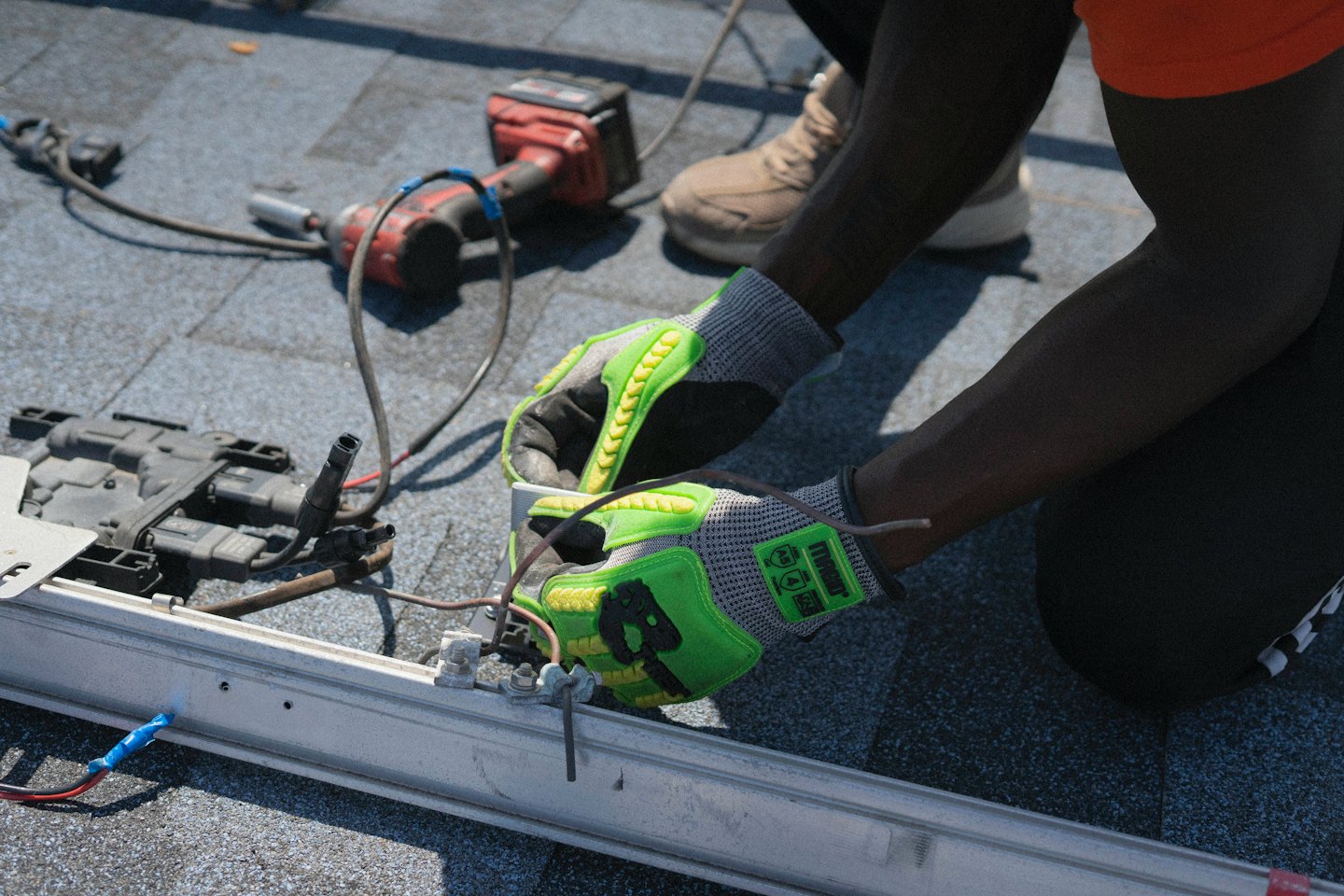Tecnico con guanti verde neon al lavoro su cavi elettrici sul tetto.
