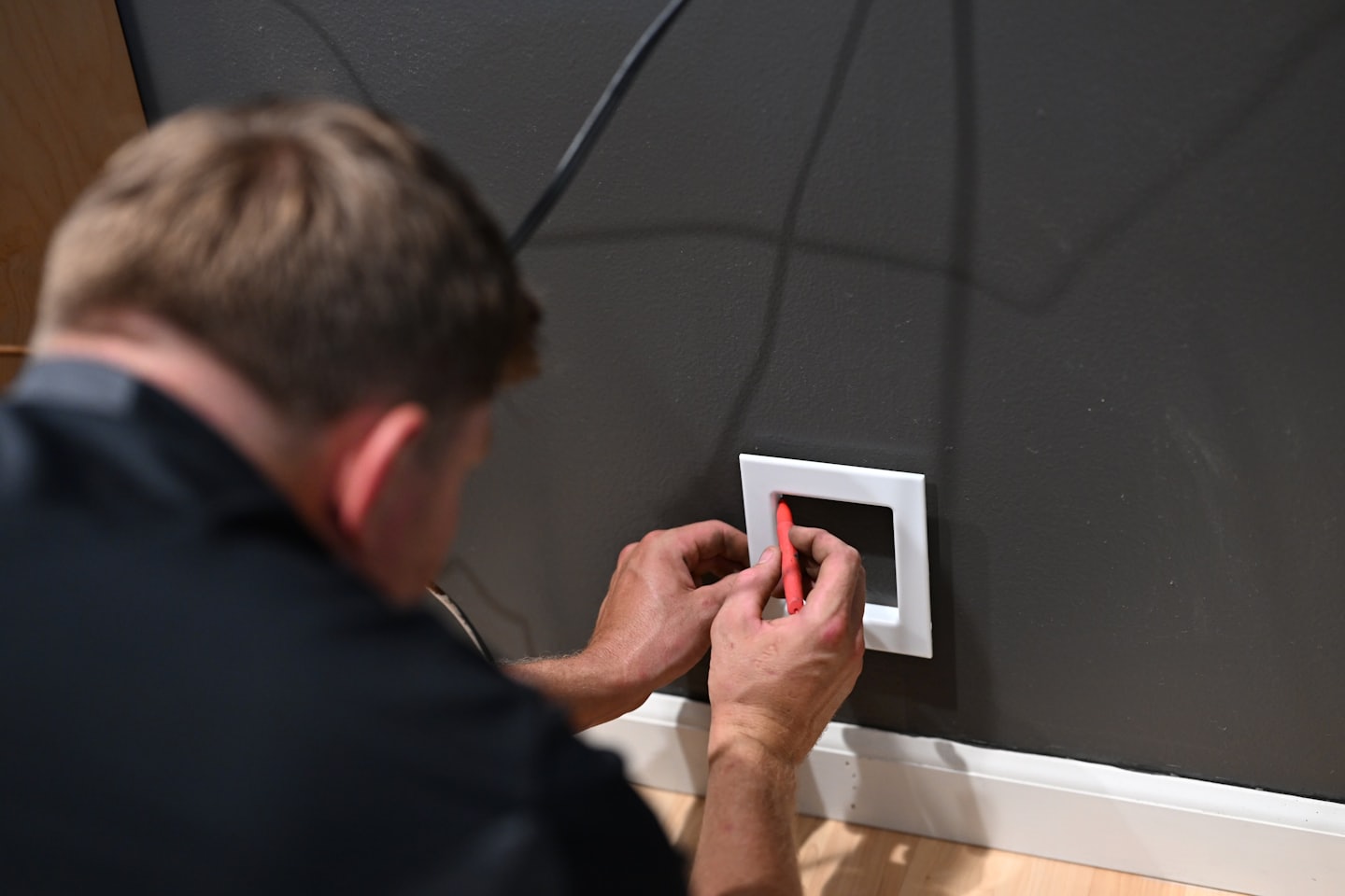 Tecnico che installa una placca a muro con uno strumento rosso.