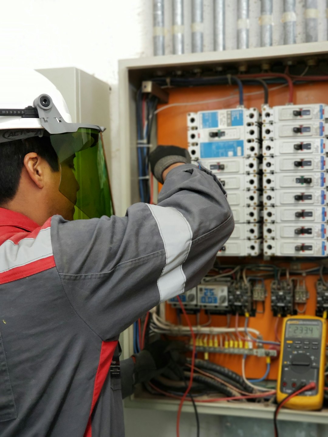 Tecnico ispeziona quadro elettrico aperto con interruttori e cavi.