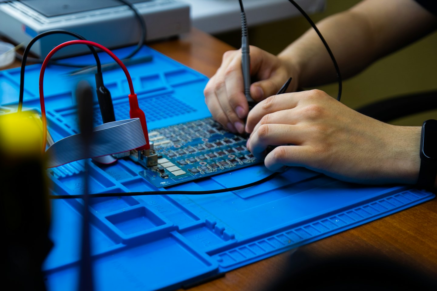 Mani che usano un multimetro per testare un circuito stampato con cavi.