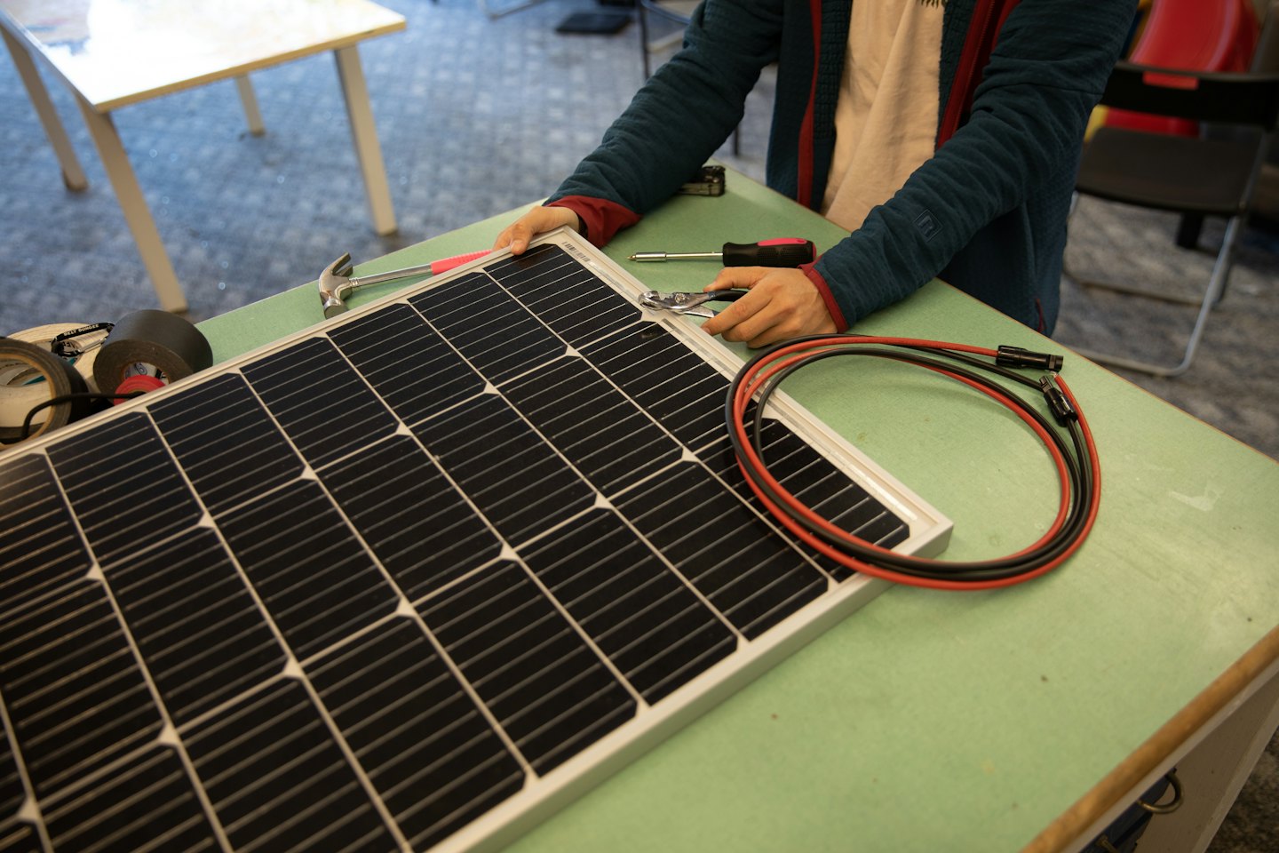 Un operaio usa una pinza per assemblare un pannello solare su un banco da lavoro.